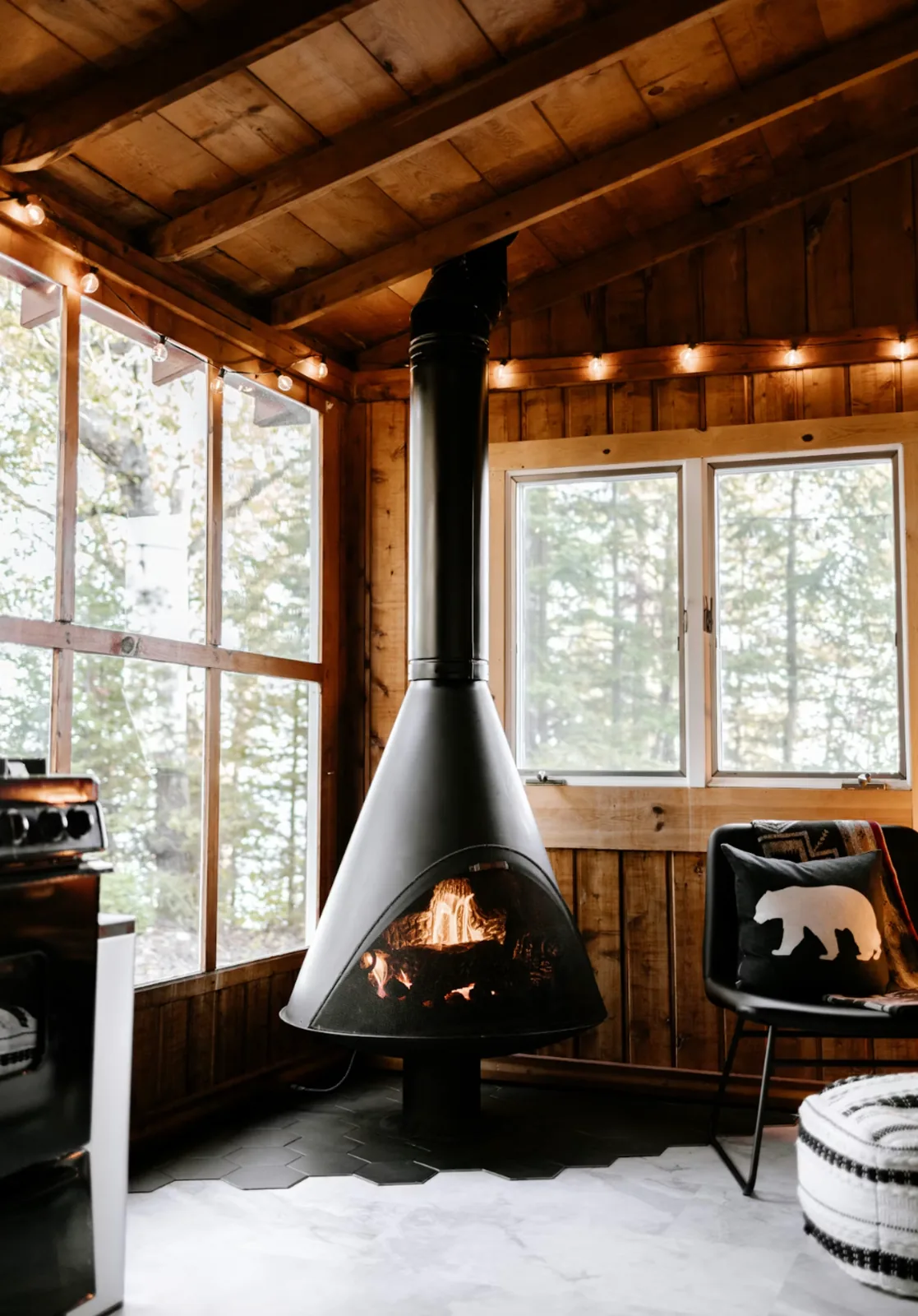 A cabin interior with a wood stove and a wall of forest glass